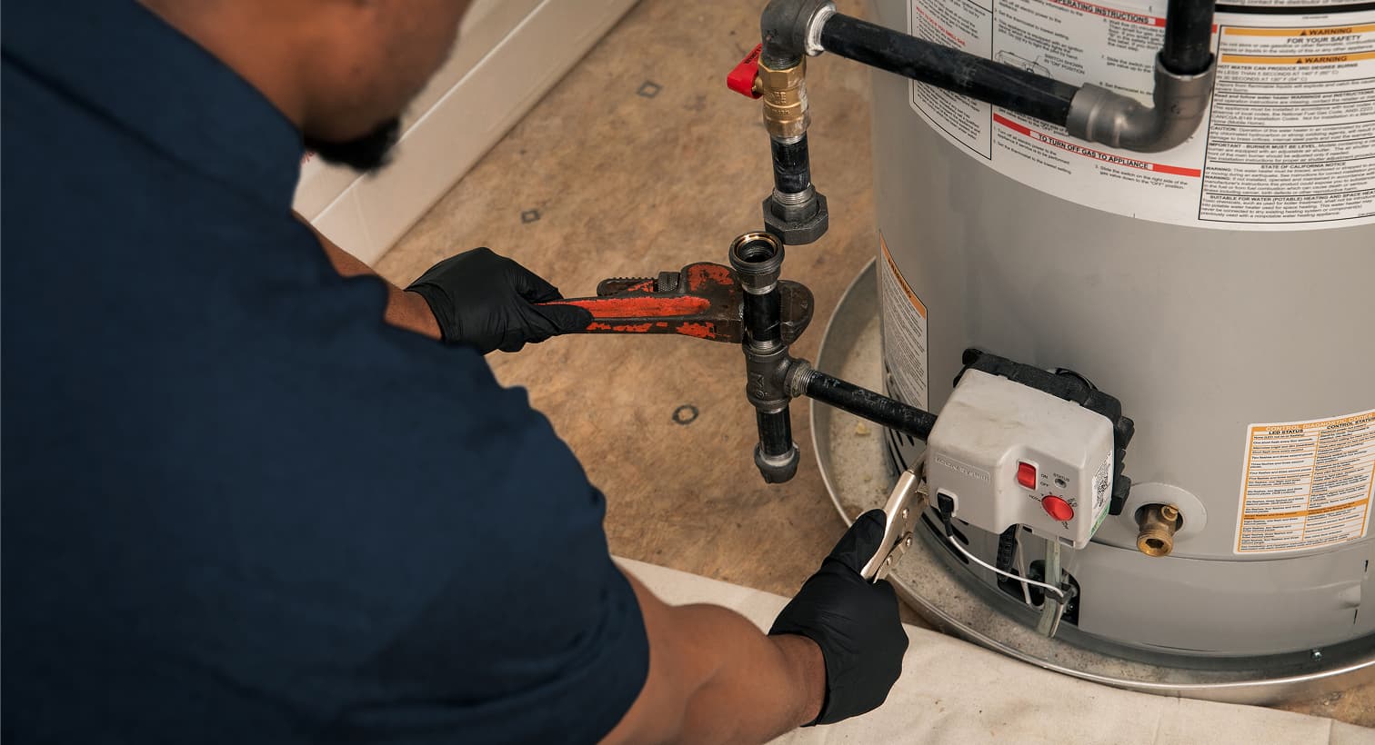 A professional Weeks plumber using a pipe wrench to fix a residential water heater during a home plumbing repair service.