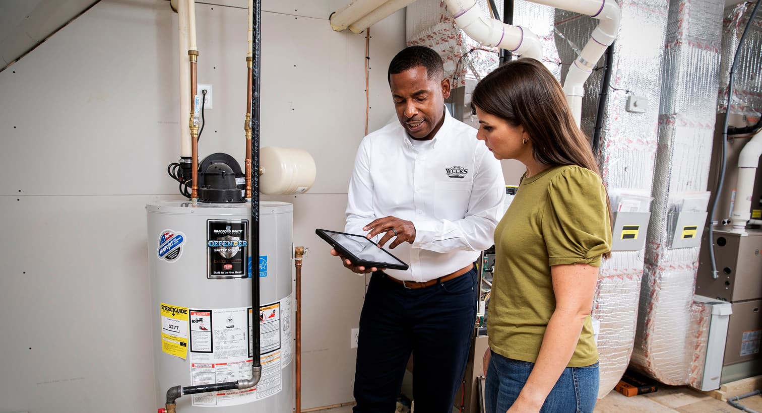 A Weeks Service Company plumber using a tablet to discuss residential water heater services, repairs, and replacement options with a homeowner.