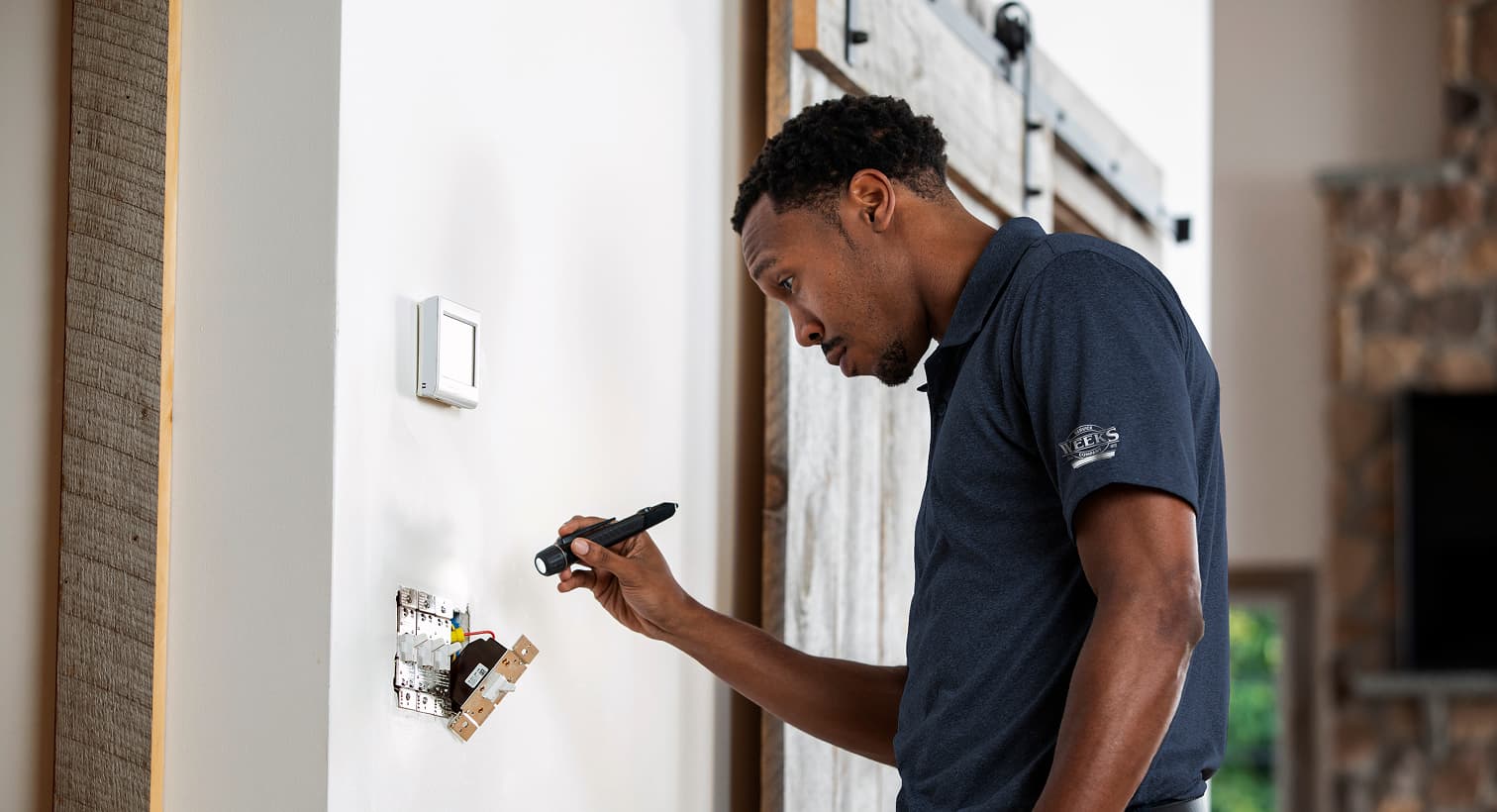 A professional Weeks Service Company electrician using a flashlight to safely inspect and troubleshoot exposed residential wall switch wiring during an electrical repair service.