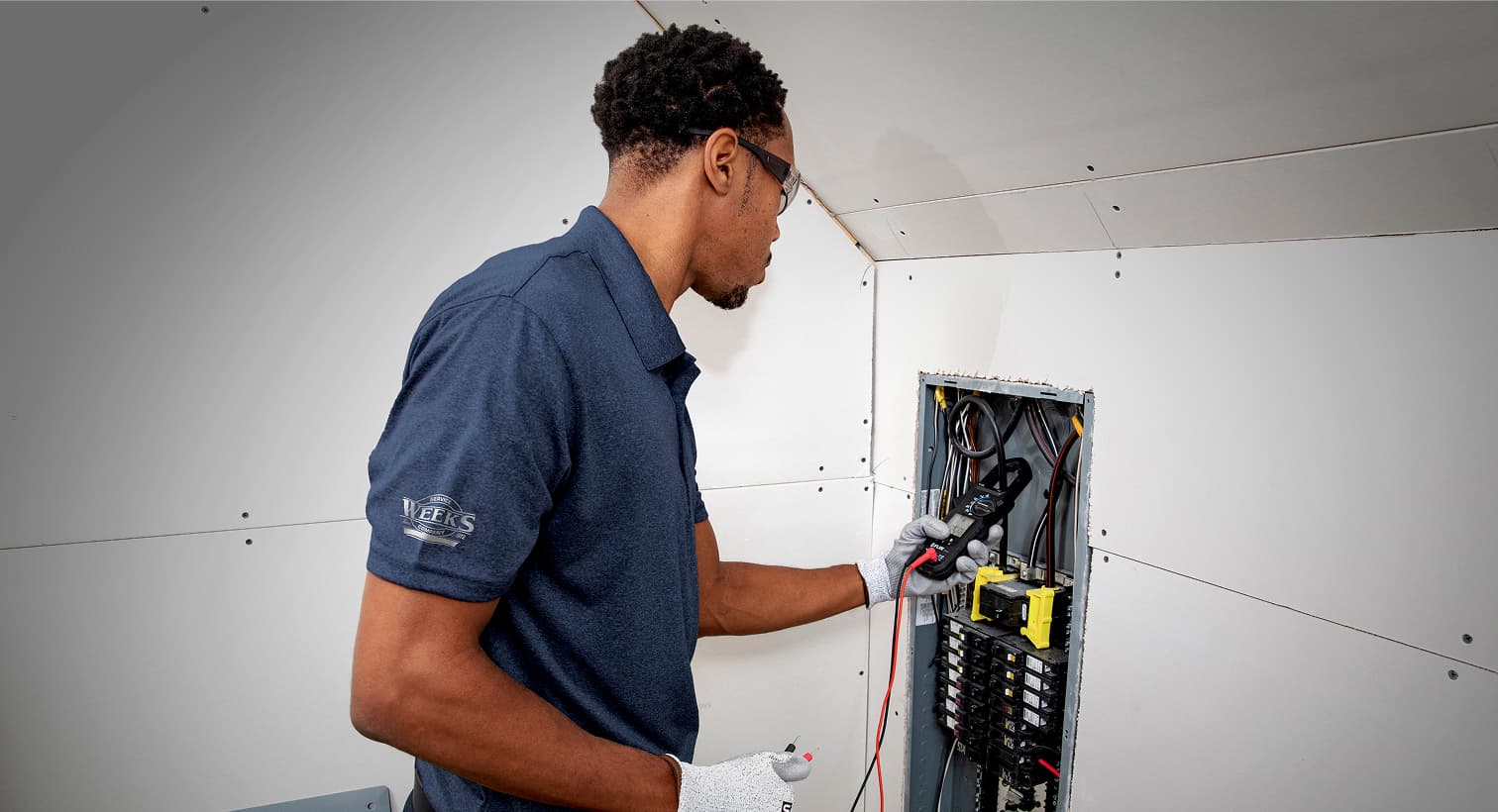 A professional Weeks Service Company electrician using a digital multimeter tool to test and inspect a residential electrical panel during a circuit breaker service call.