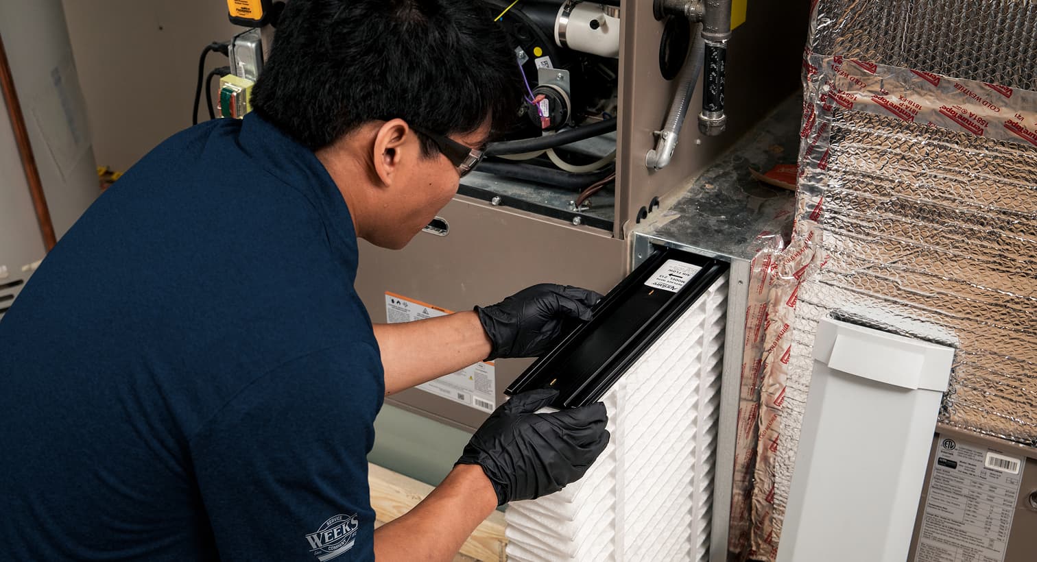 A professional Weeks HVAC technician replacing a clean pleated air filter in an indoor air handler unit during a routine AC maintenance tune-up.